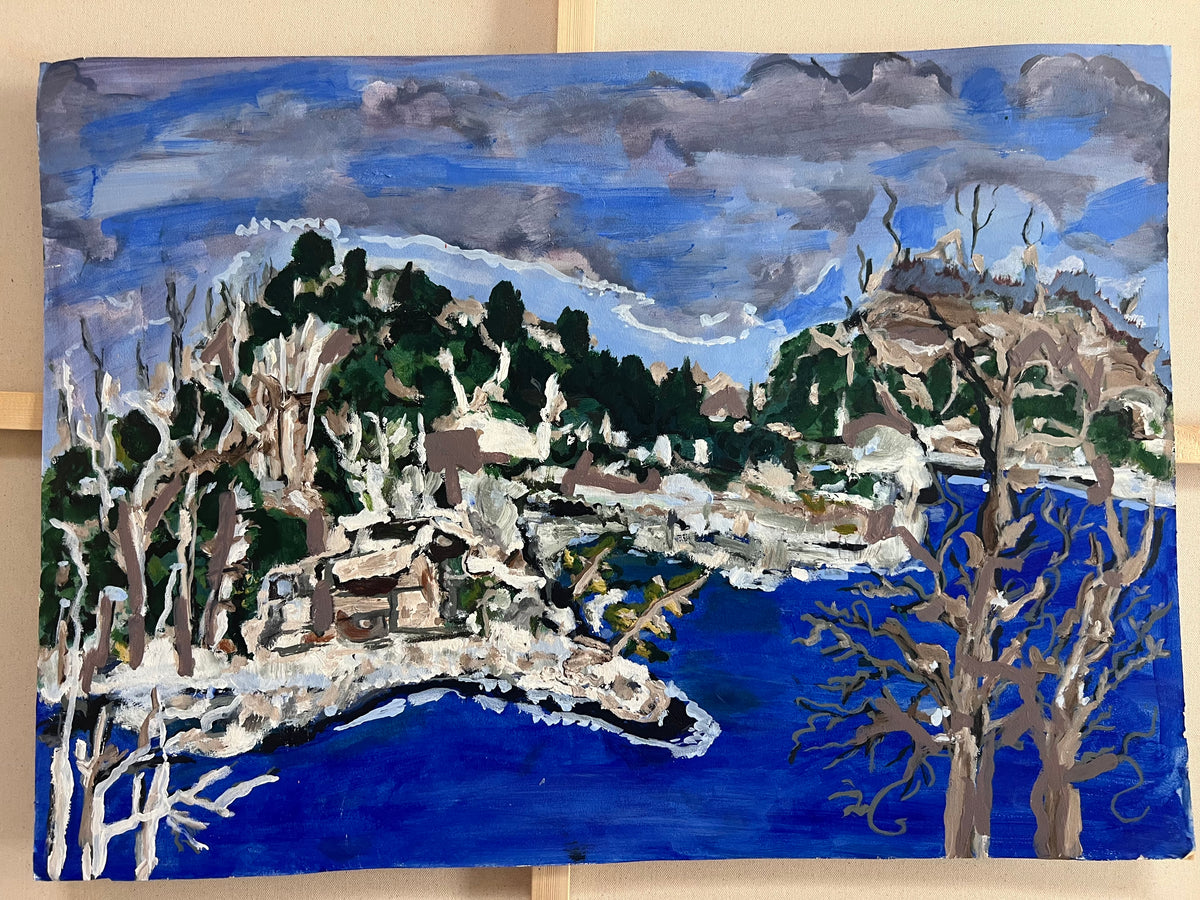 An expressive landscape painting depicting a coastal village with deep blue water, rocky shorelines, leafless trees, and a cloudy sky, shown on a light-colored wooden surface.
