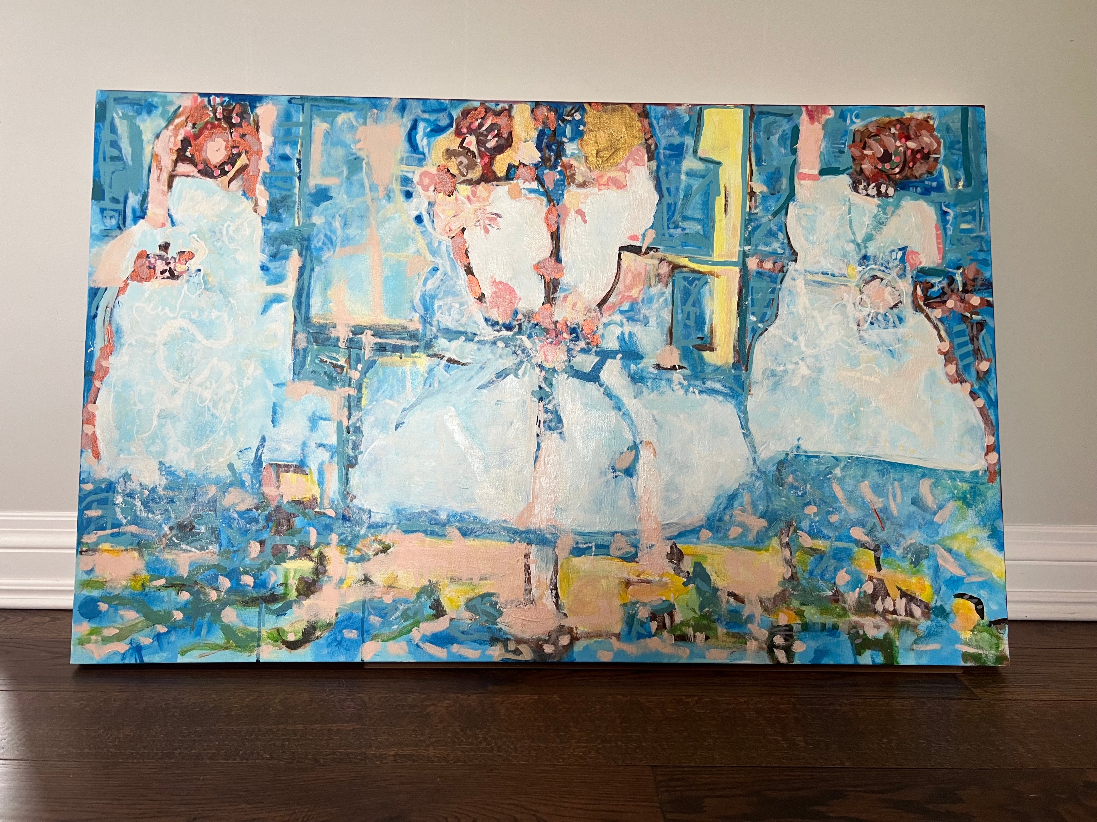 An abstract canvas painting of three women in white dresses, painted with expressive brushstrokes in shades of blue, white, yellow, and brown, leaning against a beige wall on a dark wood floor.